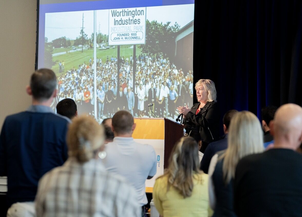 Worthington Steel employee speaking at podium on stage in front of crowd and projected screen