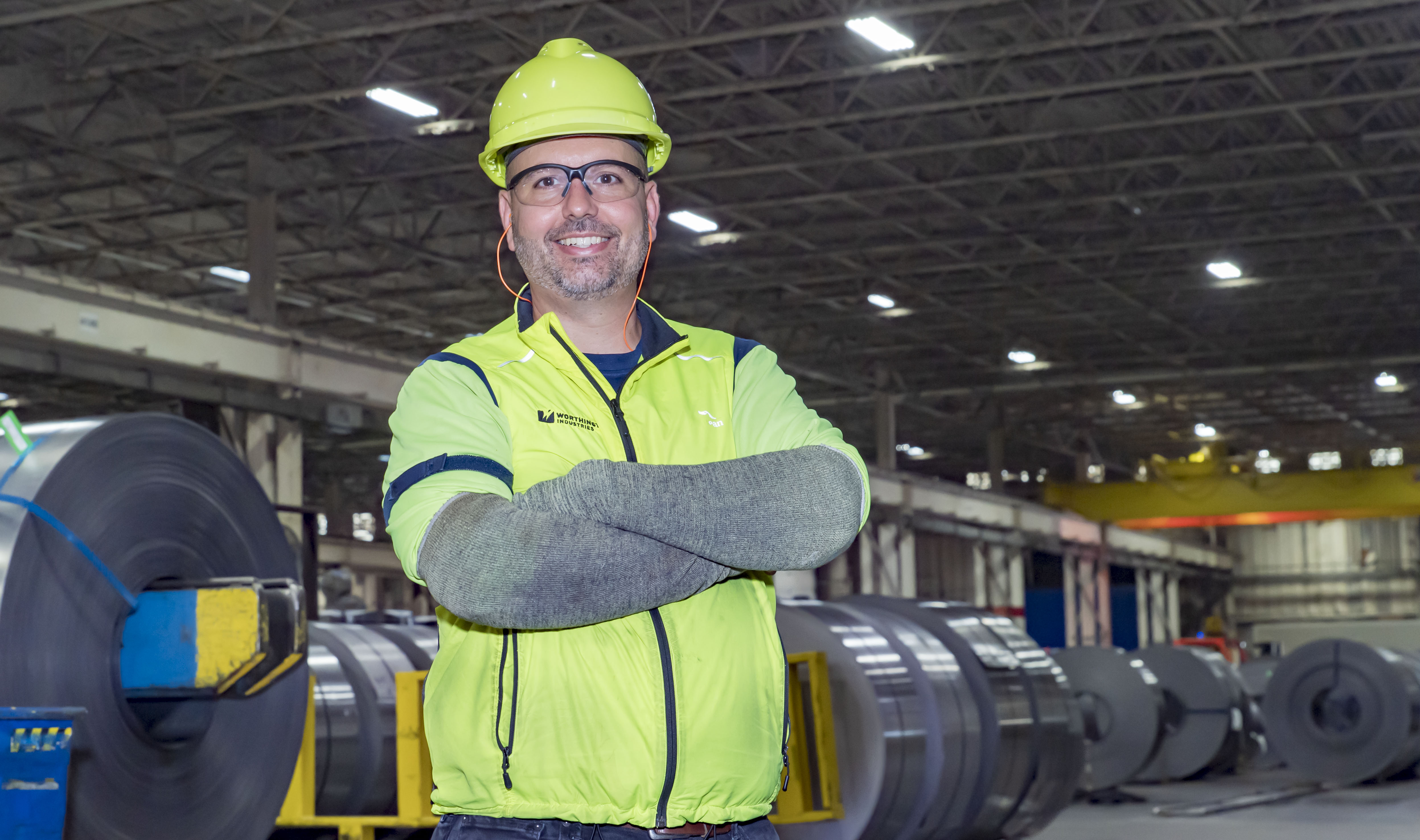 A Worthington Steel employee in PPE standing with arms crossed and smiling while in a steel facility.