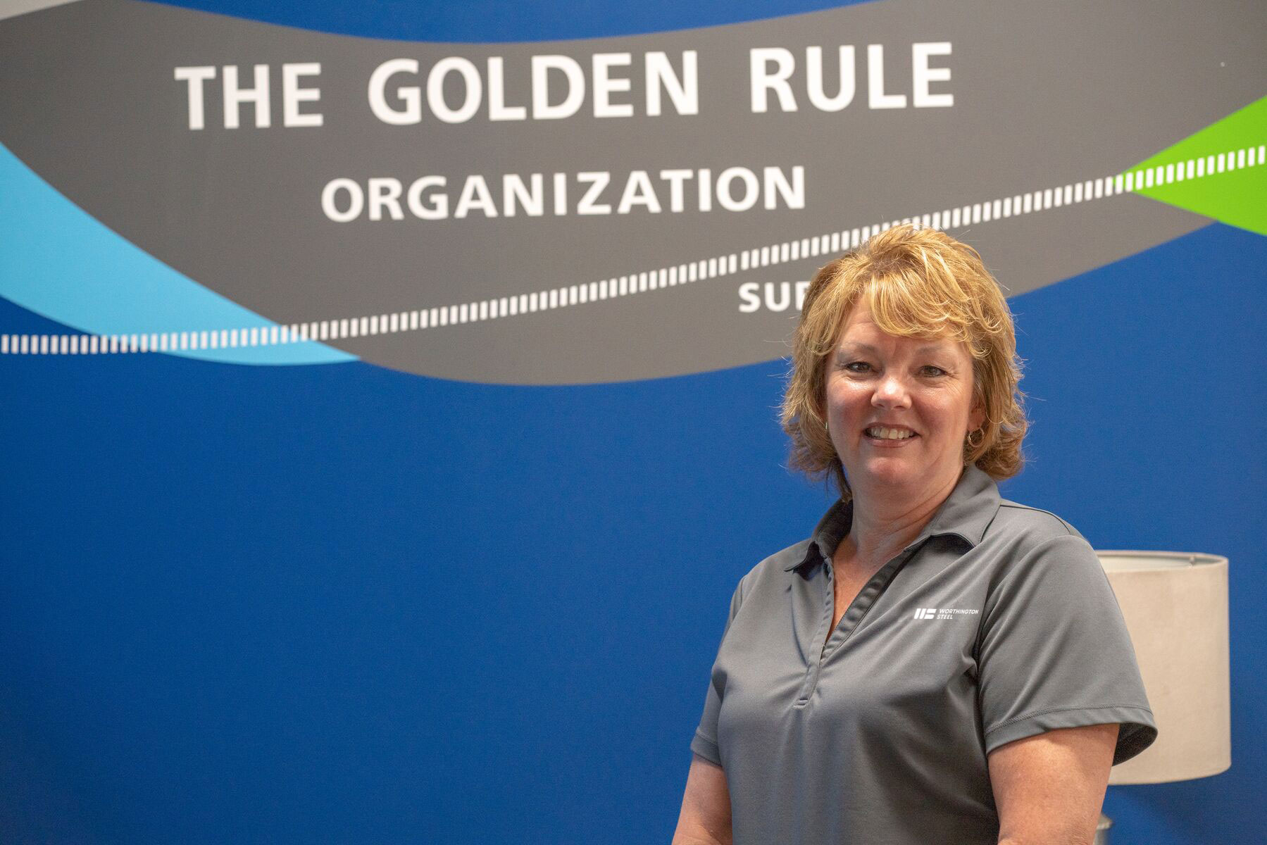 Worthington Steel employee standing in front of a wall that says "The Golden Rule Organization"