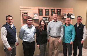 A group of Worthington Steel employees smiling at the camera in front of a wall of awards.