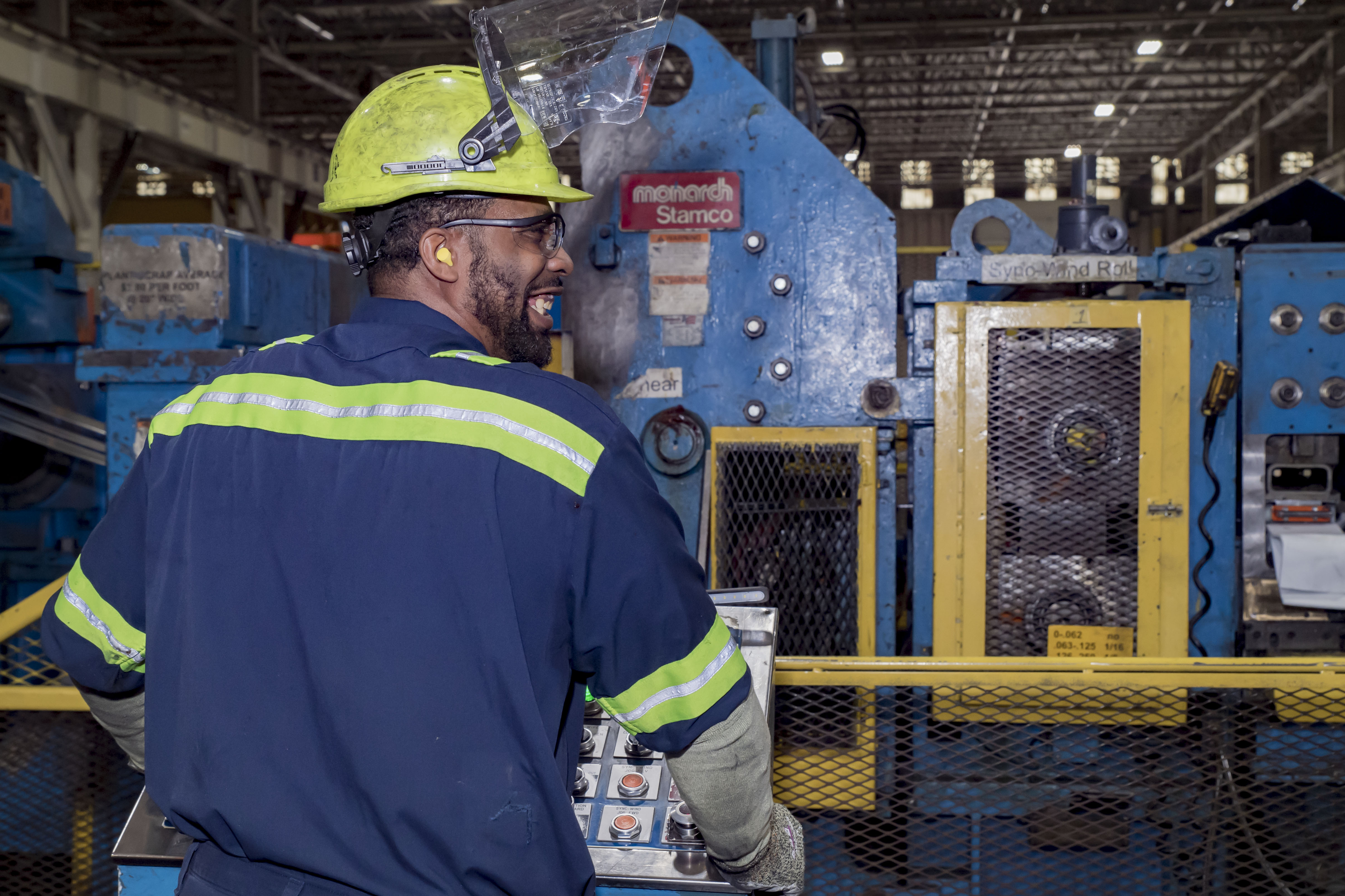 employer wearing glasses, ear plugs, helmet and gloves whole at work station