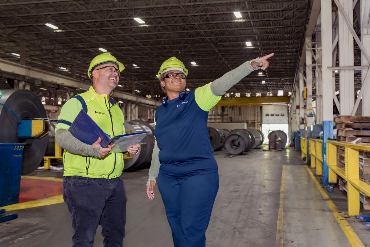 Worthington Steel employees reviewing plans and inspecting operations inside a steel processing facility.