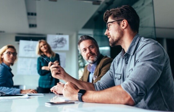 Four employees conversing in a meeting space with designs hung up behind them.