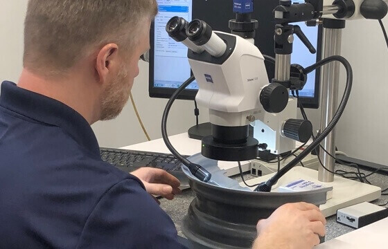 A flat roll metallurgist conducting a study on tire rims using a microscope and computer.