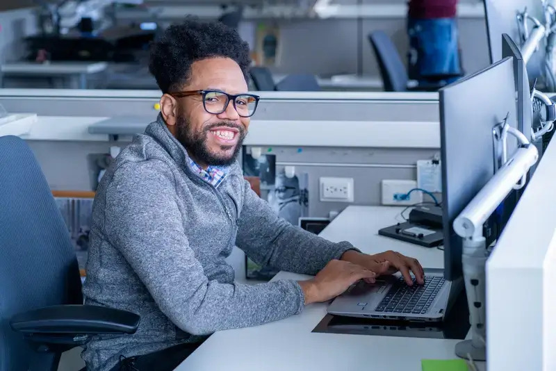 Worthington Steel employee sitting at their desk, smiling at the camera, with their hands on the keyboard.