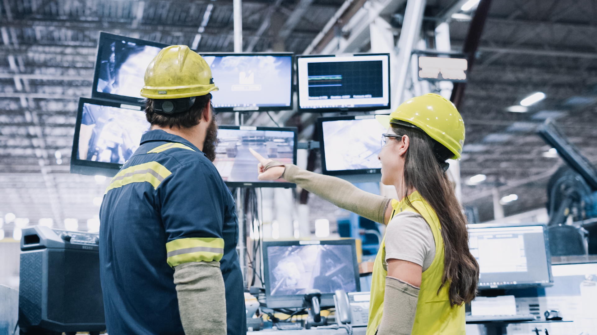 Two Worthington Steel employees reviewing production data on multiple monitors inside a steel processing facility.