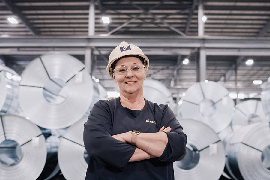 Worthington Steel employee standing confidently in front of stacked steel coils inside a processing facility.