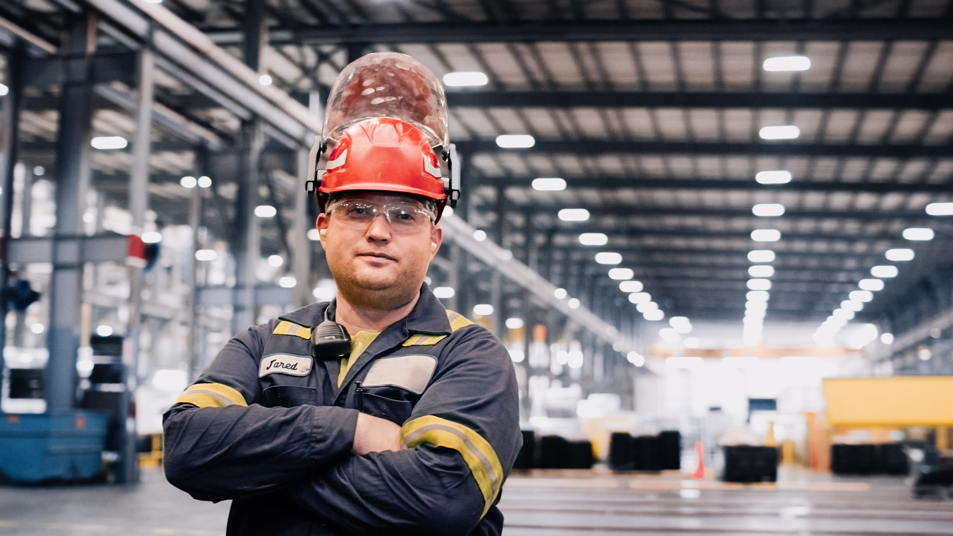 Worthington Steel employee with helmet and glasses on in a steel processing facility staring into camera.